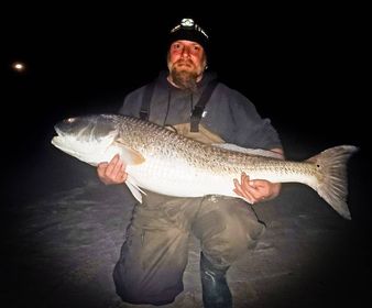 Photo of a man holding a large red drum fish at night
