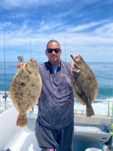 Photo of man in a boat holding two flounder
