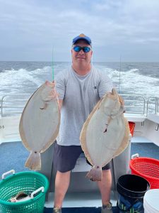 Photo of a man in a boat holding two flounder